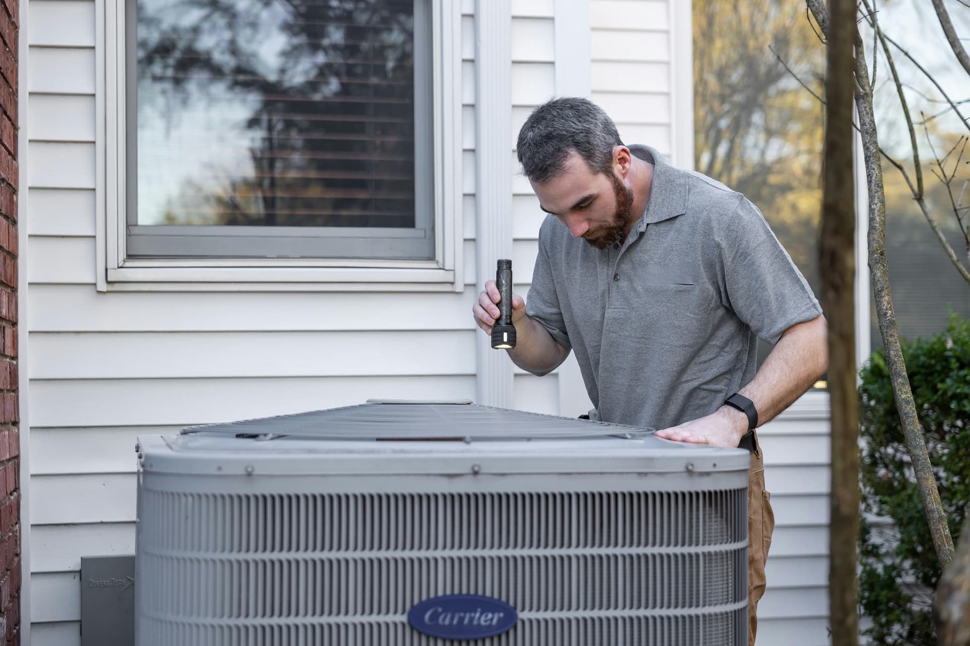 Technician inspecting a residential outdoor AC unit during install work.